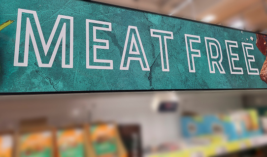 Close up color image depicting a Meat Free sign indicating the vegetarian food section inside a supermarket. Focus is on the sign, while the aisle of the supermarket is entirely defocused, allowing room for copy space.