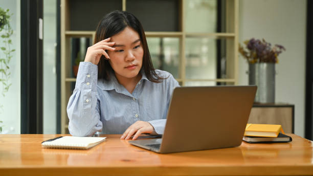 istock Frustrated female worker holding her head and looking at laptop screen, thinking find solution problem of work. 1428249735