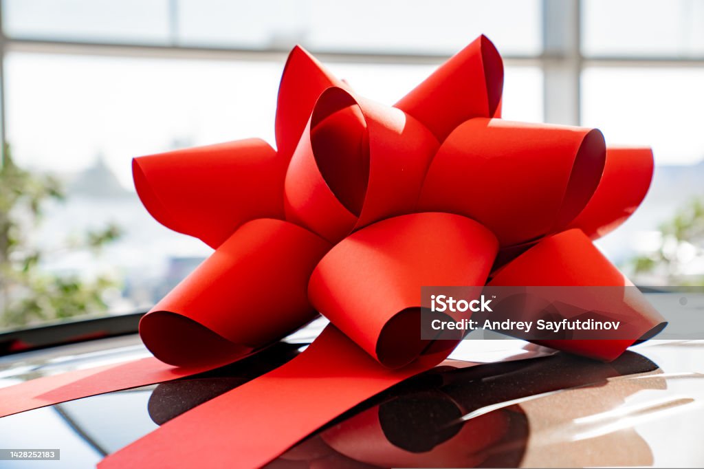 a red gift bow on the roof of a new black car in the car dealership. a red gift bow on the roof of a new black car in the car dealership. buying and selling cars. Car Stock Photo