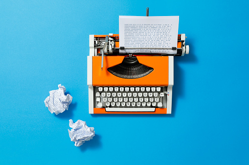Orange 70s typewriter with blue paper full of binary codes and crumpled paper