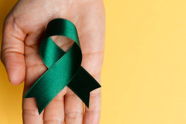 Directly above view of a hand holding green awareness ribbon over yellow background.
Some issues for what the green awareness ribbon stands for are Tissue and organ donation or transplants, mental health, mental illness, leukemia, environment, kidney neural tube defects, Save The Earth, Go Green, recycling.