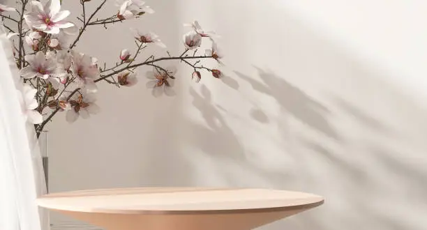 Photo of Modern and minimal cream wooden round side table and cherry blossom tree twig in vase in sunlight on beige wall background