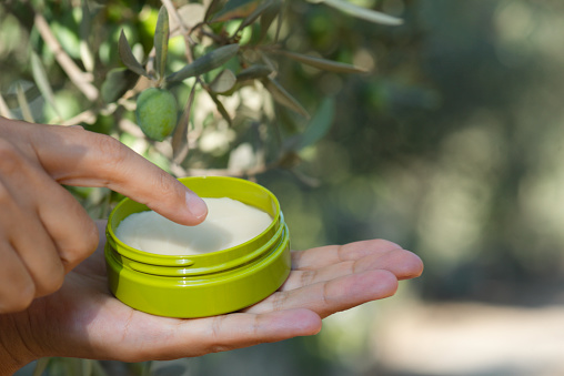 Female hand holding moisturizer in hand under olive tree branch. Representing olive fruit as  moisturizer ingredient.