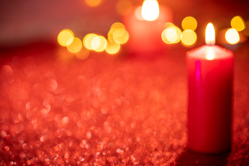 Background of glass and gold candleholder with red candles and spruce branches on red table cloth. Living room decorated with lights and candles and Christmas tree