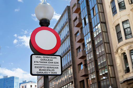 Hollow red circle sign with exceptions written below in Spanish and Basque, photographed in Bilbao, Spain, in summer