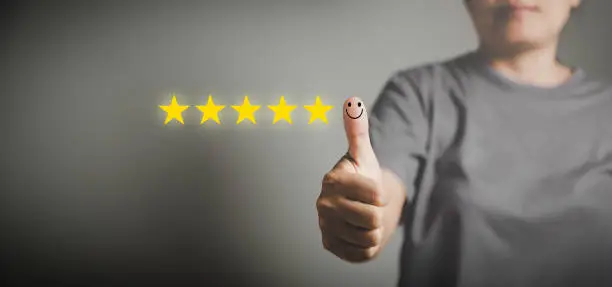 Photo of Hand with thumb up positive emotion smiley face icon and 5 star with copy space. Emotional smiley faces showing excellent satisfaction. rating very impressed. Customer service and satisfaction concept