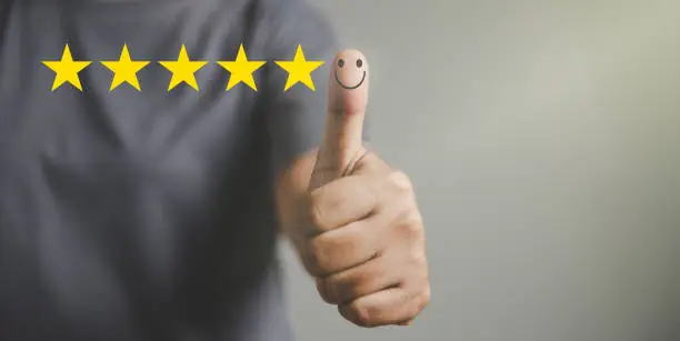 Photo of Hand with thumb up positive emotion smiley face icon and 5 star with copy space. Emotional smiley faces showing excellent satisfaction. rating very impressed. Customer service and satisfaction concept