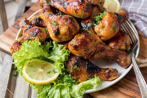 Delicious homemade marinated and glazed chicken drumsticks. Served hot and stacked on a plate isolated on wooden background