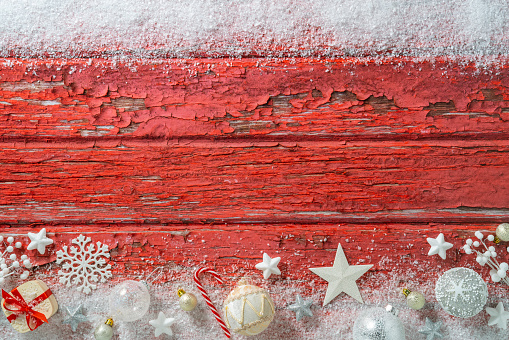 Christmas red wooden background and snow with Christmas ornaments as baubles, snowflake, fir tree, holly, candles and stars, leaving a copy space frame