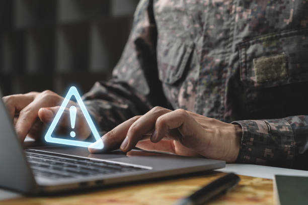 istock Soldier in camouflage uniform working on laptop with warning icon. 1428271775