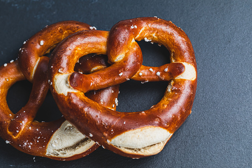 Two homemade freshly baked soft pretzels on black backround. Traditional Bavarian pretzel for Octoberfest. Top view, copy space