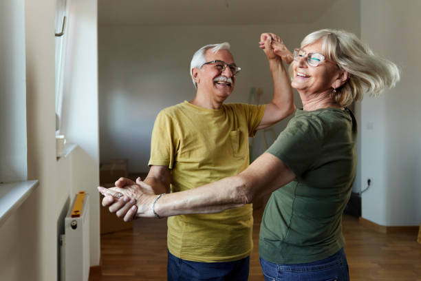Playful senior couple having fun in their new apartment. Happy mature couple having fun while holding hands and dancing after moving into a new home. middle aged couple dancing stock pictures, royalty-free photos & images