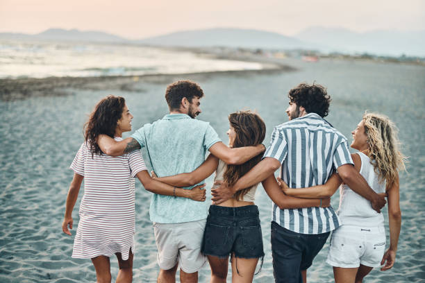 istock Back view of happy friends talking while walking embraced on the beach. 1428275178
