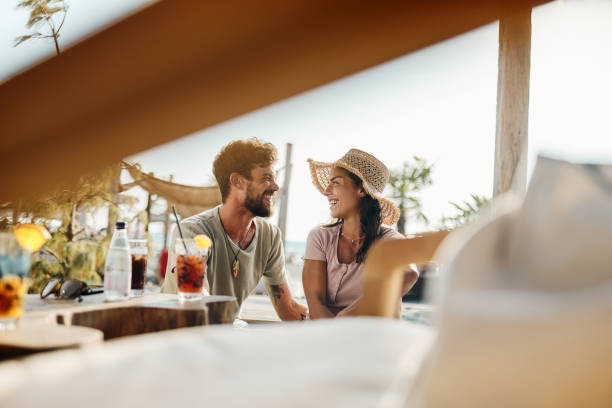 Happy couple talking while relaxing in a beach café. Young happy couple communicating while spending a summer day in a beach café. beach bar stock pictures, royalty-free photos & images