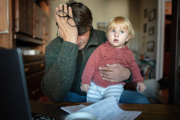 Worried man with baby girl checking bills, frustrated about high prices and having financial problems stock photo