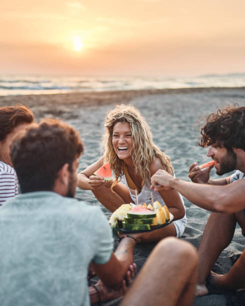Happy couples talking while eating fruit on the beach at sunset.
