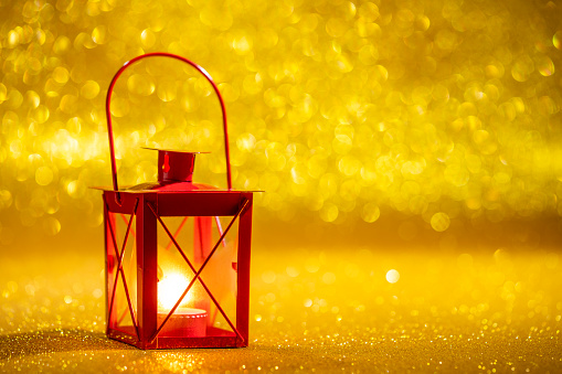 Red candle lantern in golden glitter Christmas background with blurred Christmas lights bokeh
