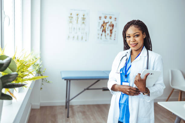 retrato de una doctora afroamericana de pie en su consultorio en la clínica - computer medical student hospital nurse fotografías e imágenes de stock