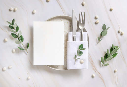 Elegant Table setting with card and envelope decorated with eucalyptus branches  top view, Wedding Mockup. Romantic table with vertical paper card. Close to nature and simplicity concepts