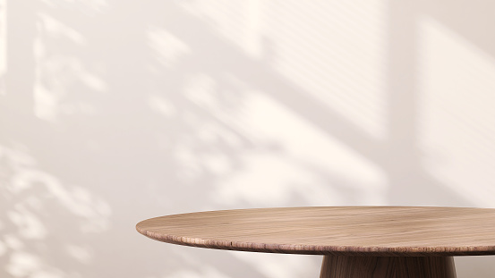 Moderna mesa auxiliar redonda de madera con luz solar desde la ventana y sombra de hoja tropical sobre fondo de pared blanco photo
