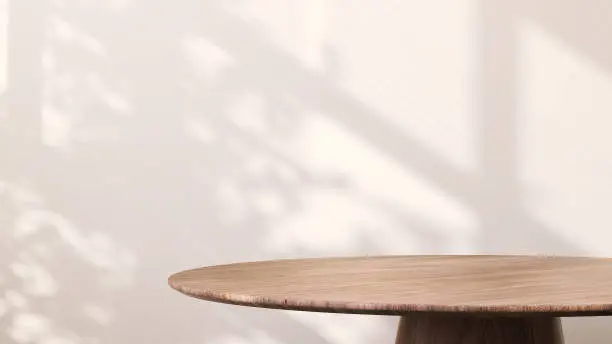 Photo of Modern round wooden side table with sunlight from window and tropical leaf shadow on white wall background