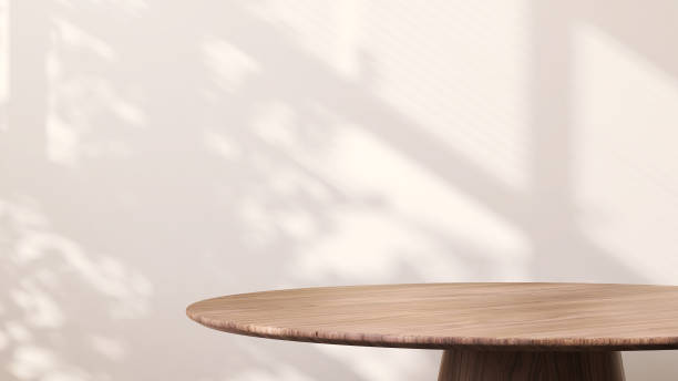 современный круглый деревянный приставной столик с солнечным светом из окна и тропической тенью листьев на белом фоне стены - side table стоковые фото и изображения