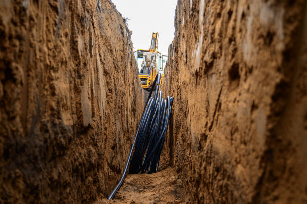 Installation of HDPE pipes in the trench. The process of laying of engineering systems water supply. Black plastic pipes underground. stock photo