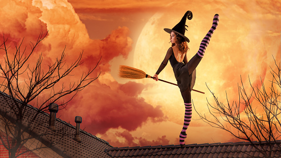 ballerina on pointe shoes in a black witch costume in a hat and with a broom dances on an orange background.