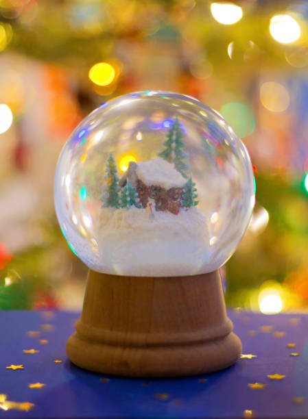 istock Snow globe with wooden house, Christmas Tree lights background 1428288499