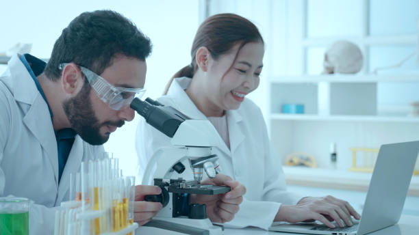 Biotechnology researcher scientist working look microscope in the medical development laboratory for vaccine development. Scientist of laboratory researcher holding medical glass bottle stock photo