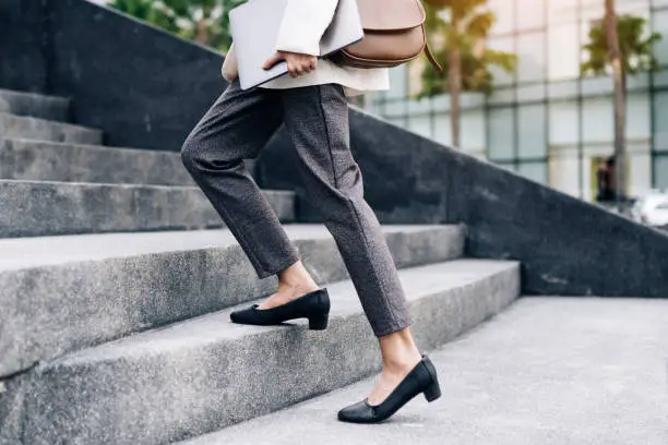 Photo of Close up legs of businesswoman hurry up walking she is late time Female business people holding laptop go to office in the modern city foot step on staircase