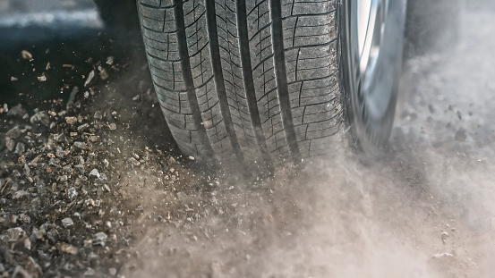 Close-up of dust and stones splashing from tire of car driving on dirt road.