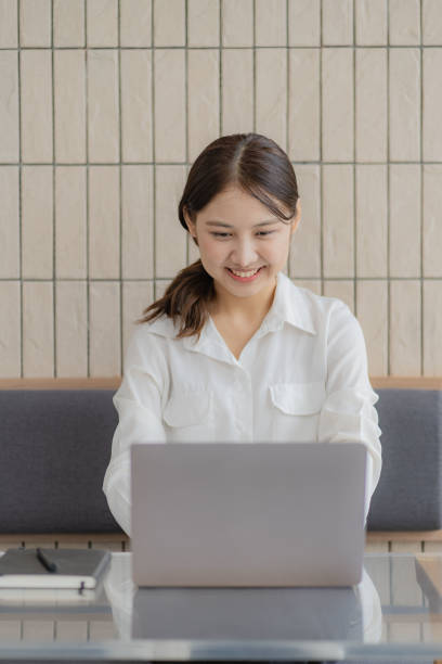 istock Beautiful Asian woman smiling happily relaxing using laptop computer in office. creative young girl working and typing on keyboard online work concept vertical picture 1428302406