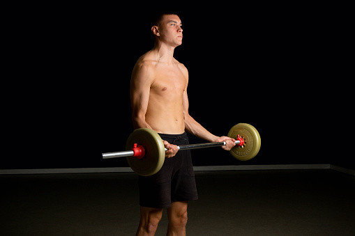 Shirtless 19 year old teenage boy excercsing his bicpes with a barbell