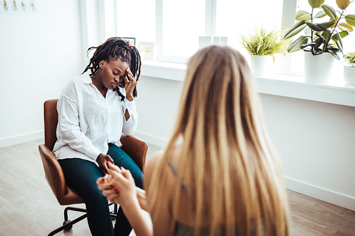 Psychotherapy session, woman talking to his psychologist in the studio. Young woman visiting therapist counselor. Girl feeling depressed, unhappy and hopeless, needs assistance. Serious disease, unwilling pregnancy