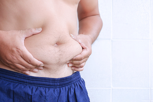 Close up of adult man hand holding excessive belly fat on white tile wall background, side view with copy space