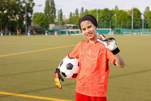 Girl with goalkeeper gloves holding the ball looking at the camera