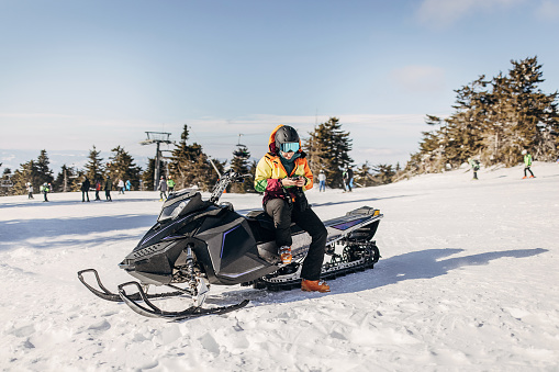 One woman, female sitting on snowmobile on the hill on a snowcapped mountain. She is using smart phone.