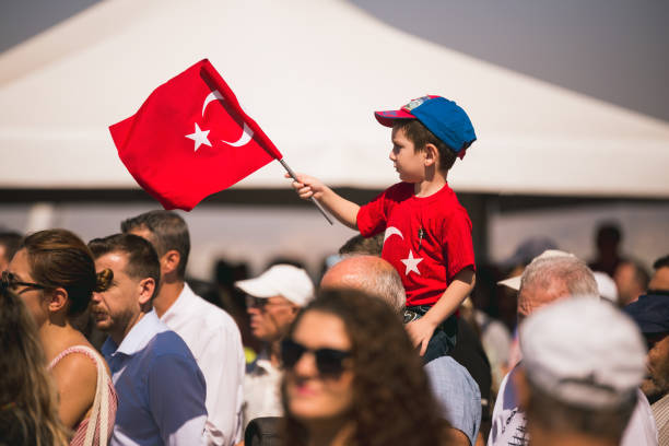 A boy with a Turkish flag and t-shirt on an adult's shoulders on the liberation day of Izmir, Turkey at Republic square Konak Alsancak. stock photo