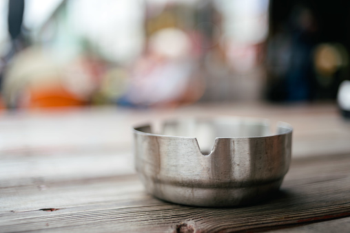 Metallic silver  shiny ashtray on a top of wooden table with blurred background