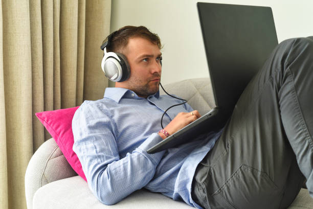 Young man beat maker working from home with his laptop laying on couch stock photo