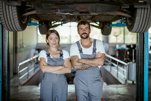Two happy auto service center employees portrait inside workshop looking at camera