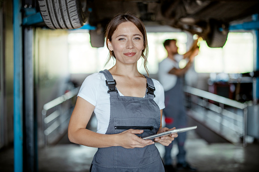 Happy female mechanic standing by the car and looking at camera