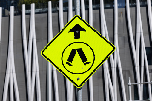 Close- up on a yellow metal street sign alerting drivers to a pedestrian crossing.