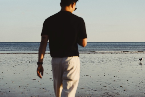 A closeup of a man walking in a black t-shirt towards the sea.