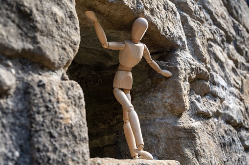 A wooden artist's figure standing, looking out of a stone building. Concept of an uncertain future, worry and concern.