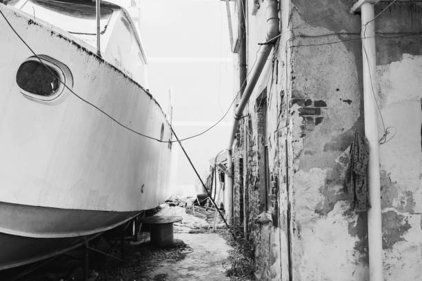 A low-angle grayscale of a ship and an abandoned building sky in the background