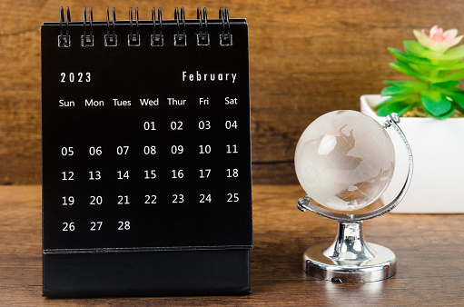 February 2023 desk calendar for 2023 year Black color with a crystal globe against a wooden table background.