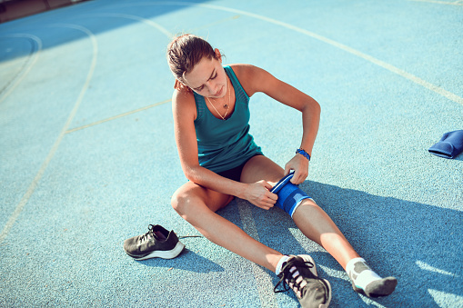 Female Bandaging Her Knee Before Running On Track