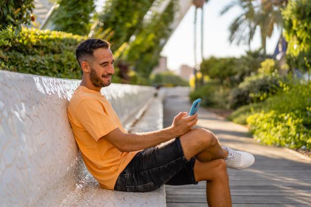 istock oung hispanic man wearing casual clothes sitting on a bench using his mobile phone smiling. 1428366991